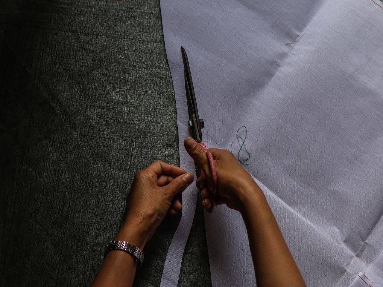 A tailor's hands using large scissors to cut white fabric for a traditional wedding dress.